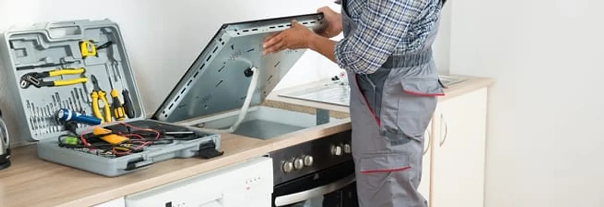 Cooktop repair technician lifting a built-in stovetop for service in Boulder, CO