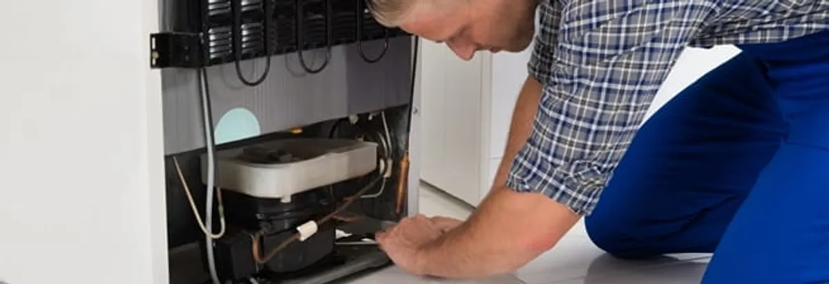Refrigerator repair technician servicing the compressor and condenser area in Boulder, CO
